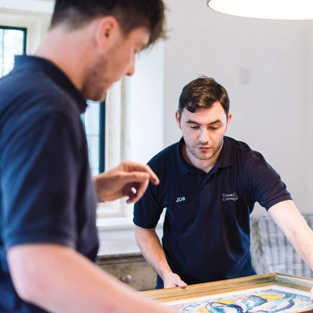 Two removal men packaging a piece of fine art on a table